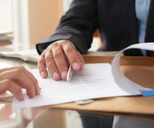 Close-up of businessman examining business contract and signing it at the office desk