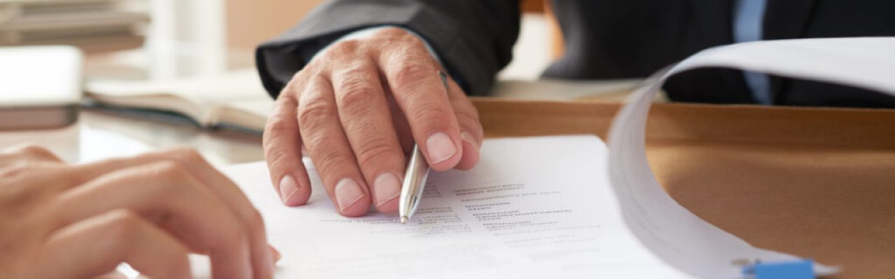 Close-up of businessman examining business contract and signing it at the office desk